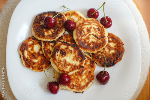 Curd cheesecakes on a white plate with red cherries Summer picture with summer associations. Inspiration for photographers. With space for text. Ideas for desserts and baking