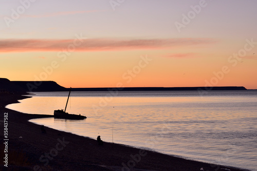 Vista de bote hundido y pescador en la orilla al atardecer