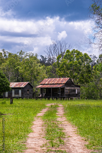 Disused wooden homestead surrounded by grazing field and dramatic stormy sky in Kroombit Tops National Park, Queensland
