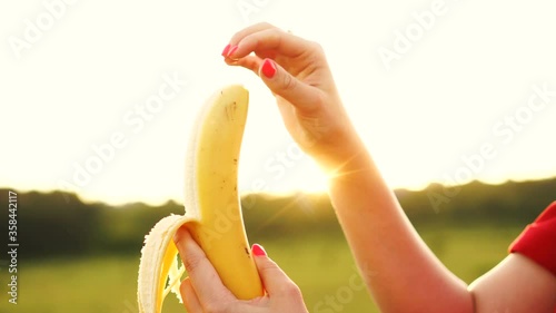 Woman peeling and biting the banana. Ripe yammy banana in female hands on sunset background