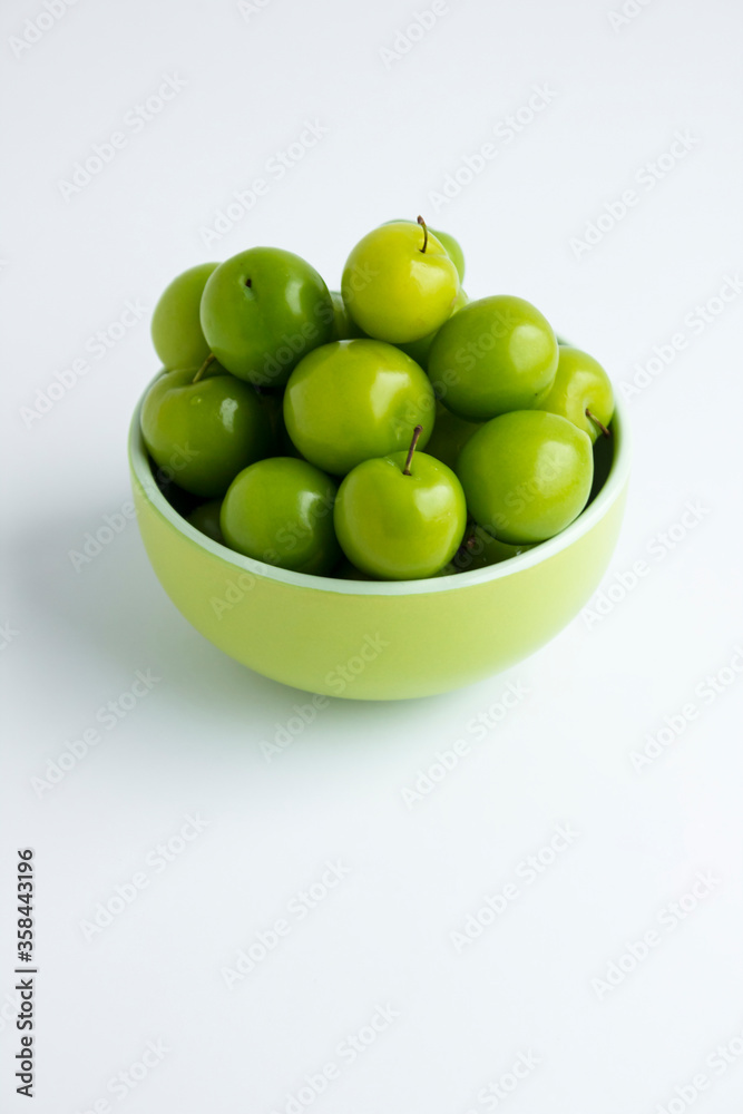 Ripe,fresh green plums in the green color bowl on the white surface with copy space.Vertical image.