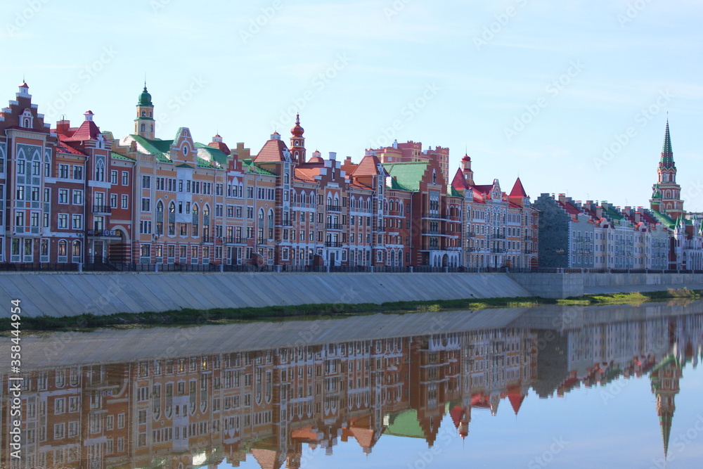 Town house stands on the river bank and is reflected in the water on a summer morning