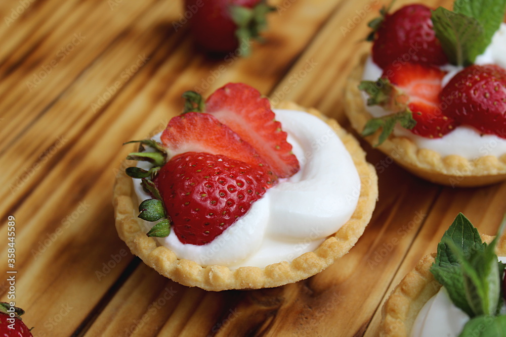 Tartlets with cream and strawberries on a wooden table