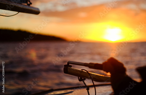 Detail of rodder and skipper's hand on small sailing boat in vast seascape at sunset between Bird Island and Turkey Beach, Queensland photo