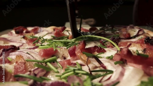 Roller blade cutting isolated baked Tarte flambee french style pizza topped with cheese, onion, tomatoes and green chives, black background, macro detail pull back photo