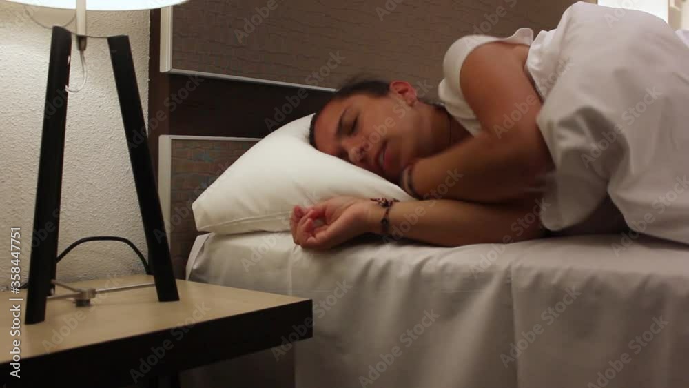 Young woman tossing and turning in bed to find comfortable sleep position with lights on