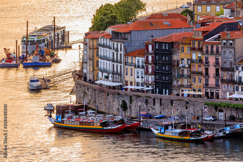 Facades of traditional colorful houses in Ribeira and rabelo boats on Douro at sunset golden hour in Porto, Portugal