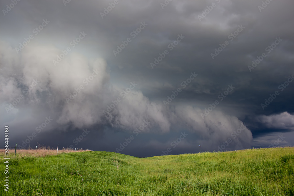 A dark storm advances, featuring a ragged shelf cloud with rain and hail behind it.