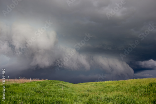 A dark storm advances, featuring a ragged shelf cloud with rain and hail behind it.