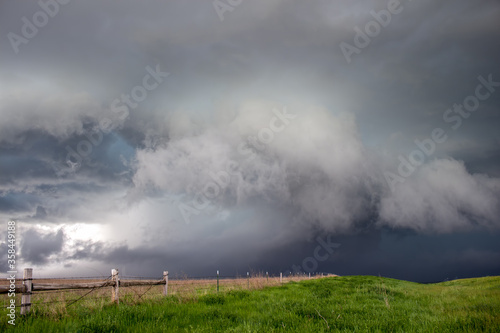 A dark storm advances  featuring a ragged shelf cloud with rain and hail behind it.