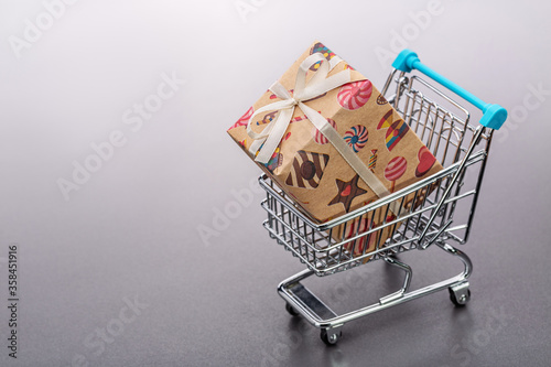 Toy shopping cart with gift in large color box. Gray background.