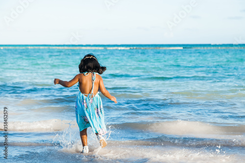 Little girl in beautiful blue dress enjoying white sandy caribbean tropical beach jumping running and having fun in the ocean sea waves 