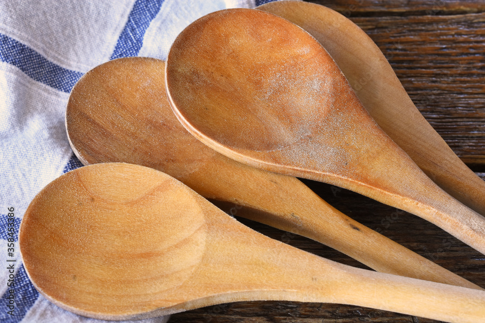 A close up image of several wooden mixing spoons and a blue and white dish towel. A close up image of several wooden mixing spoons and a blue and white dish towel.