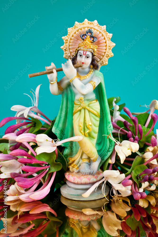 Hindu god Krishna. Statue with flowers on a blue background.