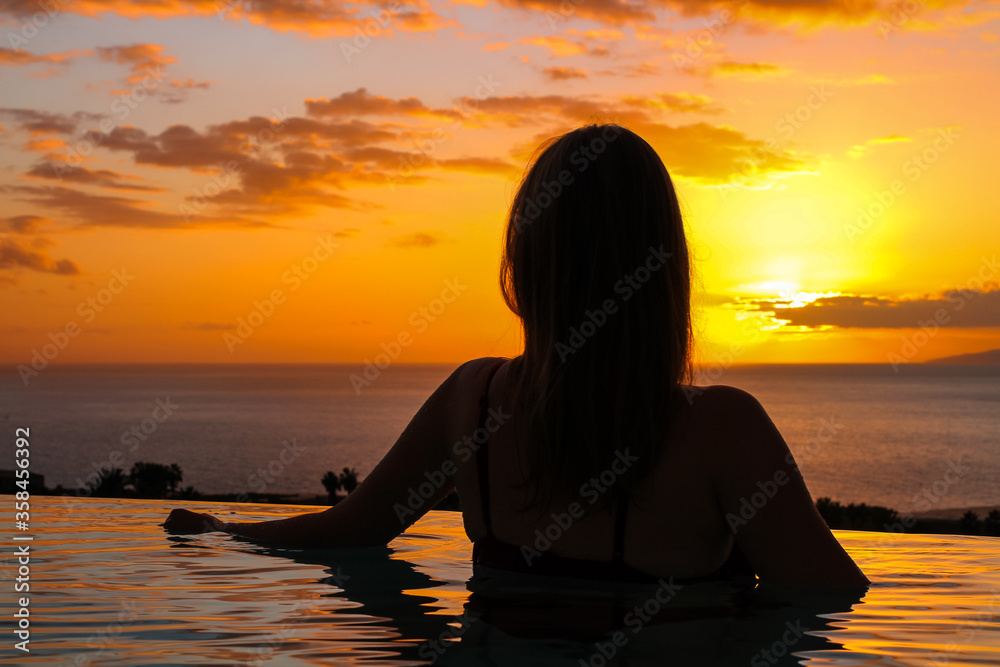 Girl with a half-back in the pool against the backdrop of the ocean and sunset