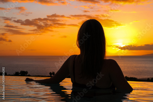 Girl with a half-back in the pool against the backdrop of the ocean and sunset