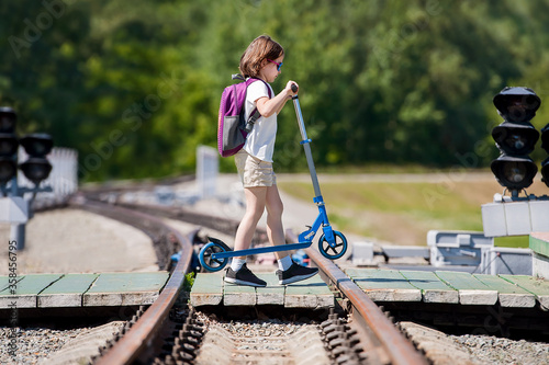 Crossing the railway tracks made of wood across the railway tracks in the daytime. Schoolgirl carrying scooter and crossing road. Pedestrian passing a crosswalk. Safety concept for road users