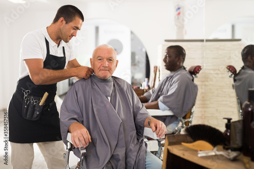 Barber putting on hairdresser cloak to elderly male client