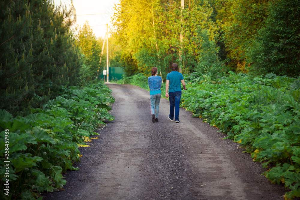 A man and a woman walk along a forest road towards the sun. A man and a woman walk along a forest road towards the sun.