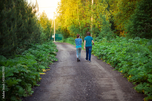 A man and a woman walk along a forest road towards the sun.