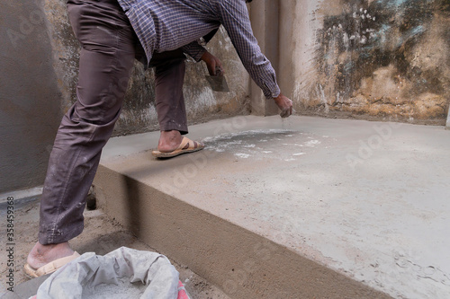 Indian labour levelliing plastered floor using flat trowel and distributing cement manually by hand, Stock image.