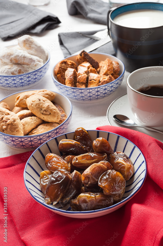 Vertical shot of plate of delicious and highly nutritious dates on a breakfast table with napkins, food and drinks on the background. Ramadan essential food stills.