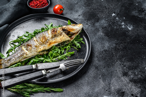 Baked sea Bass fish with arugula, grilled seabass. Black background. Top view. Copy space