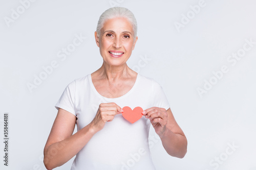 Portrait of charming lady holding papercard heart on her breast looking at camera isolated over white background photo