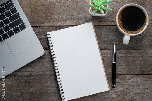 Top view from above of Blank open notebook, laptop with pen and coffee cup on wood table background. Workplace creative at home. Flat lay, Business-finance or education concept with copy space.