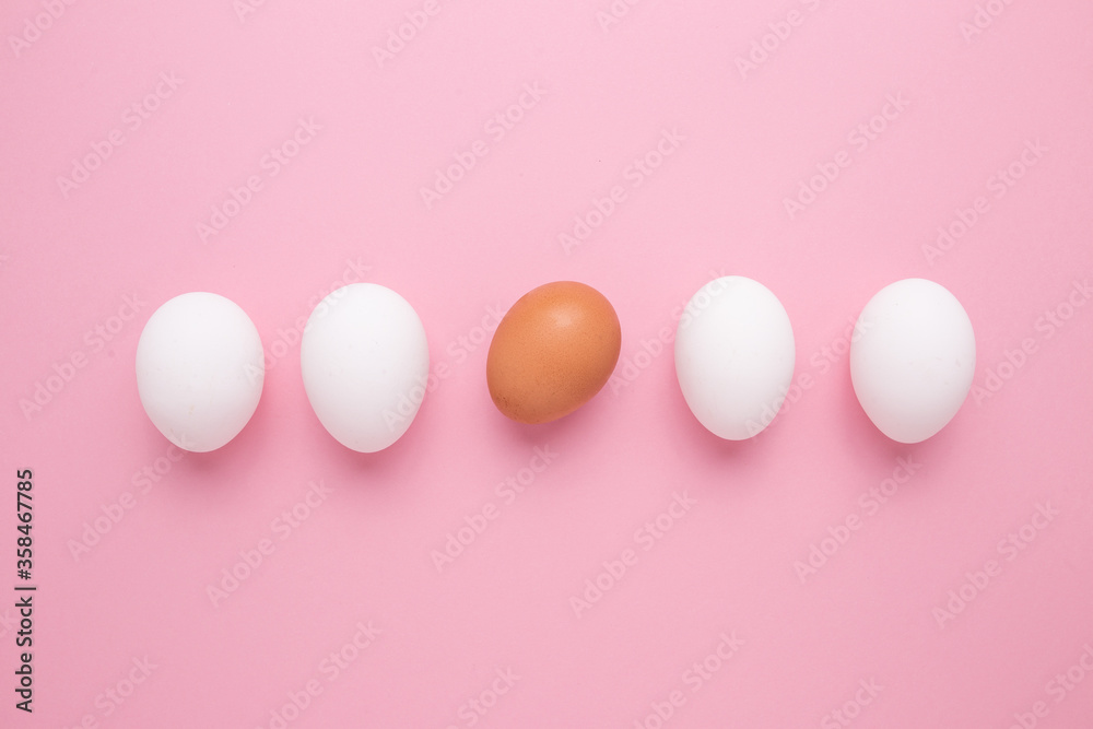 The concept of personality. Brown egg among white eggs on a pink background.