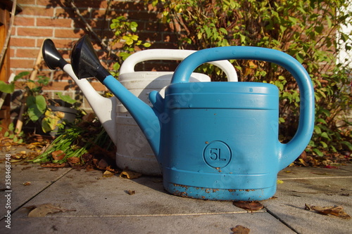 Fotografia Two plastic watering cans in the garden in autumn