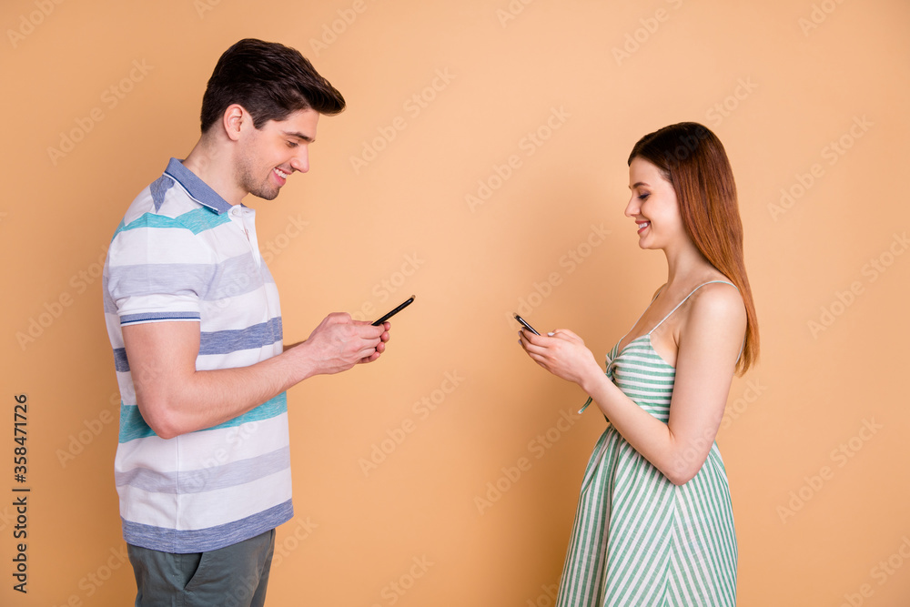 Profile side view portrait of his he her she nice attractive focused cheerful cheery couple using digital device wi-fi 5g app isolated over beige pastel color background Profile side view portrait of his he her she nice attractive focused cheerful cheery couple using digital device wi-fi 5g app isolated over beige pastel color background