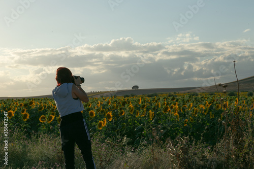 Joven viajera haciendo foto a campo de girasoles al atardecer
