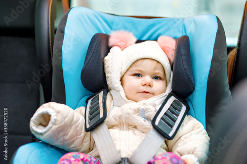 Adorable baby girl with blue eyes sitting in car seat. Toddler child in winter clothes going on family vacations and jorney. Safe travel, children safety, transportation concept.