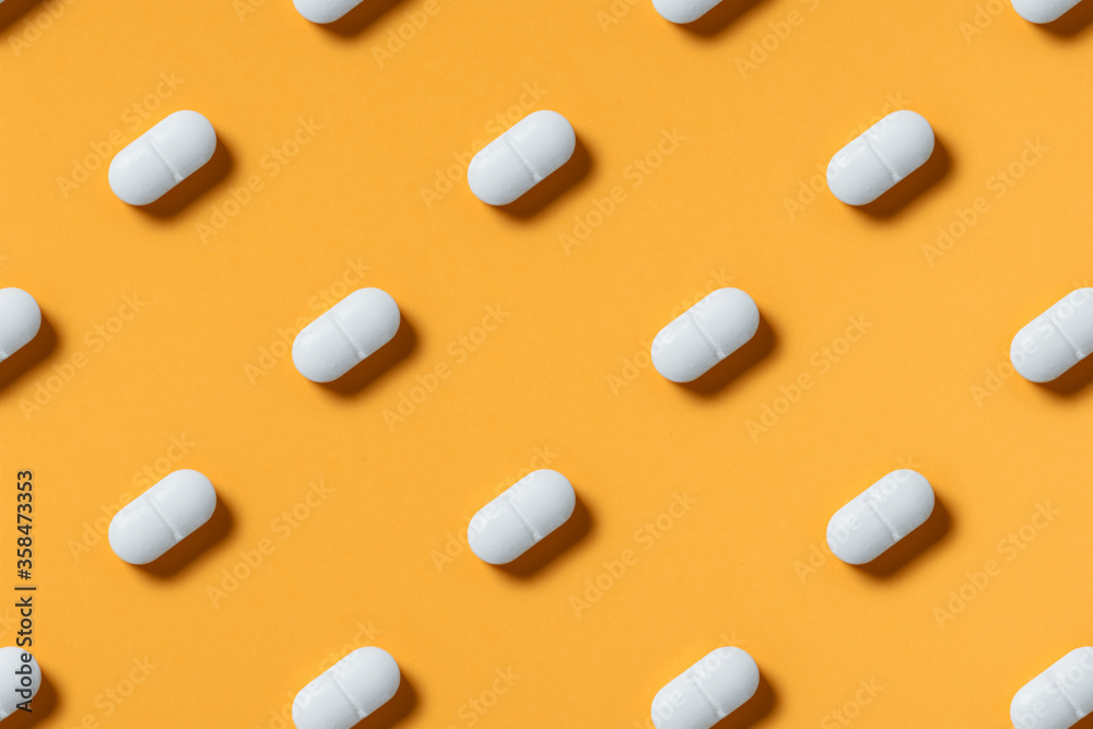 White pills or capsules lie in rows diagonal on orange background top view copy space pattern.