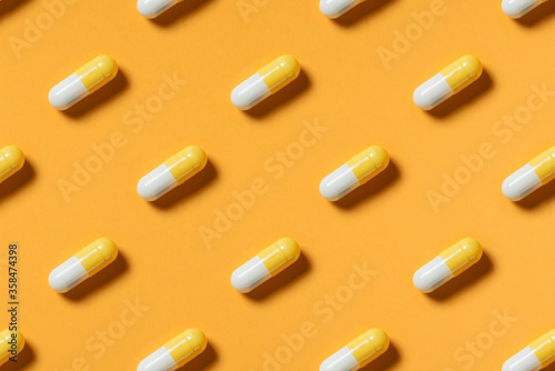 Yellow white pills or capsules lie in rows diagonal on orange background top view copy space pattern.