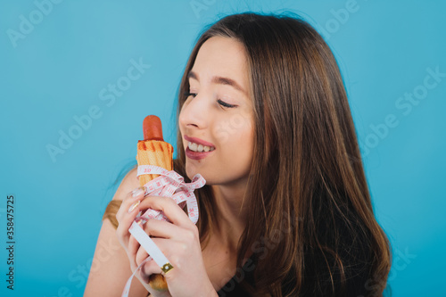 girl holds hot dog in hand with measuring tape on blue background