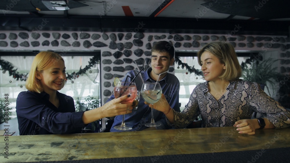 Two women and one man are sitting at the bar counter and drinking cocktails Two women and one man are sitting at the bar counter and drinking cocktails