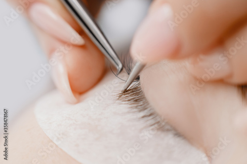 Macro photo Eyelash extension procedure. Master tweezers fake long lashes beautiful female eyes