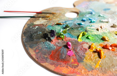 Colorful palette with oil paints and paint brushes on a white background