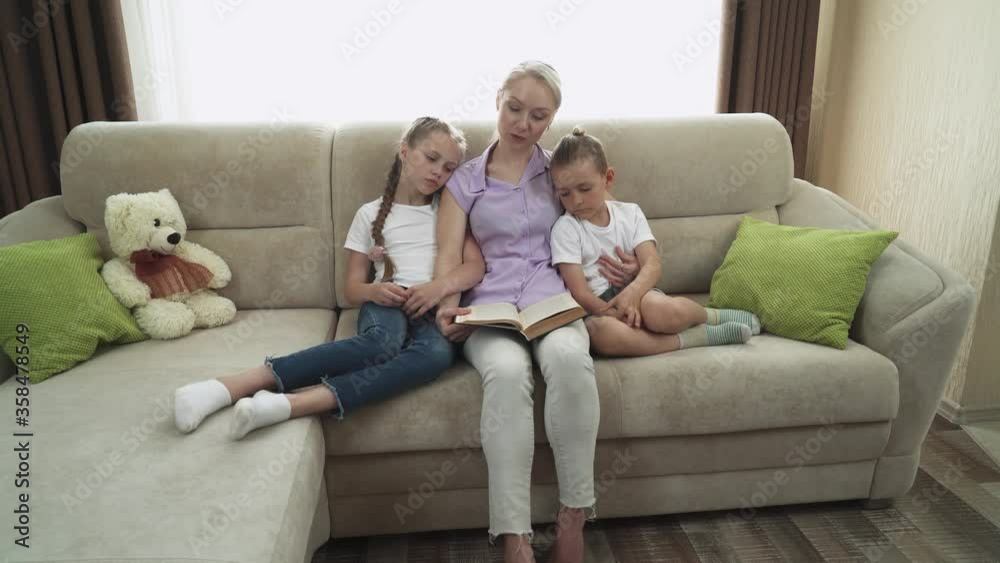 Motherhood, mother reads a fairy tale to her children, read a book, daughter and son sit next to mother on the sofa and listen. Motherhood, mother reads a fairy tale to her children, read a book, daughter and son sit next to mother on the sofa and listen.