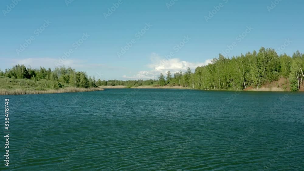 Ripples on a lake in Tula oblast drone aerial shot in summer time. High quality 4k footage of drone flying up above lake surrounded by green trees and forest under bright blue sky Ripples on a lake in Tula oblast drone aerial shot in summer time. High quality 4k footage of drone flying up above lake surrounded by green trees and forest under bright blue sky