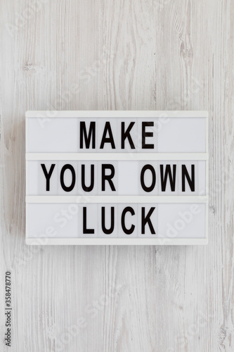 'Make your own luck' on a lightbox on a white wooden surface, top view. Flat lay, from above, overhead.