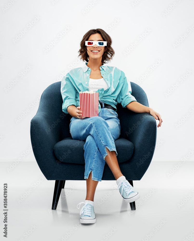© Syda Productions - comfort, people and furniture concept - portrait of happy smiling young woman in 3d movie glasses with popcorn in striped bucket sitting in modern armchair over grey background