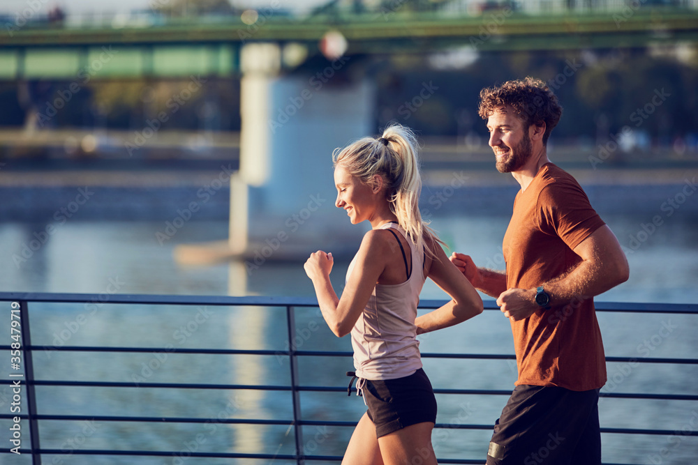Obraz premium Modern woman and man jogging / exercising in urban surroundings near the river.