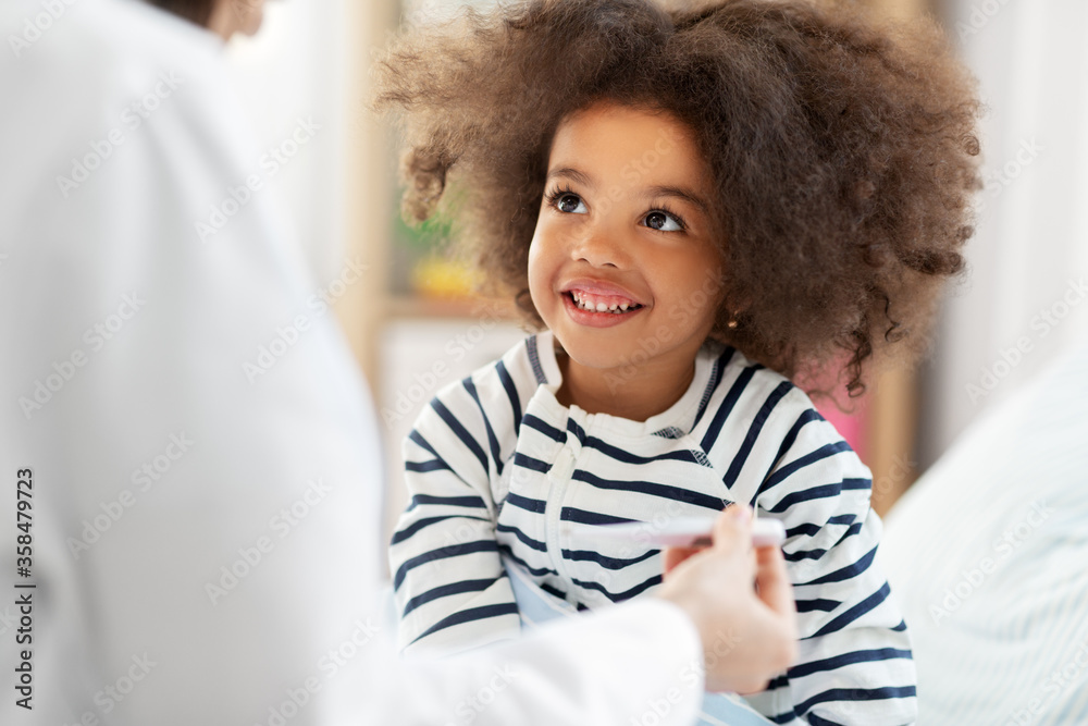 healthcare, medicine and people concept - doctor showing thermometer to happy smiling sick little african american girl in bed at home healthcare, medicine and people concept - doctor showing thermometer to happy smiling sick little african american girl in bed at home