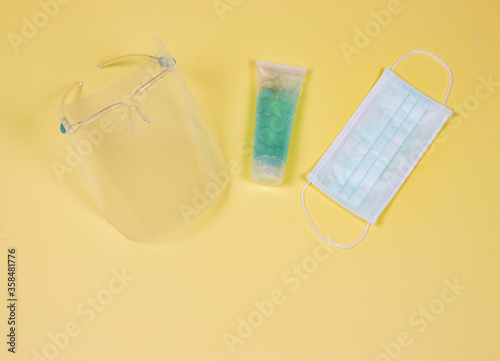 COVID-19 prevention and new normal lifestyle concept. Top view of face shied , alcohol hand sanitizer gel and surgical face mask on yellow background.