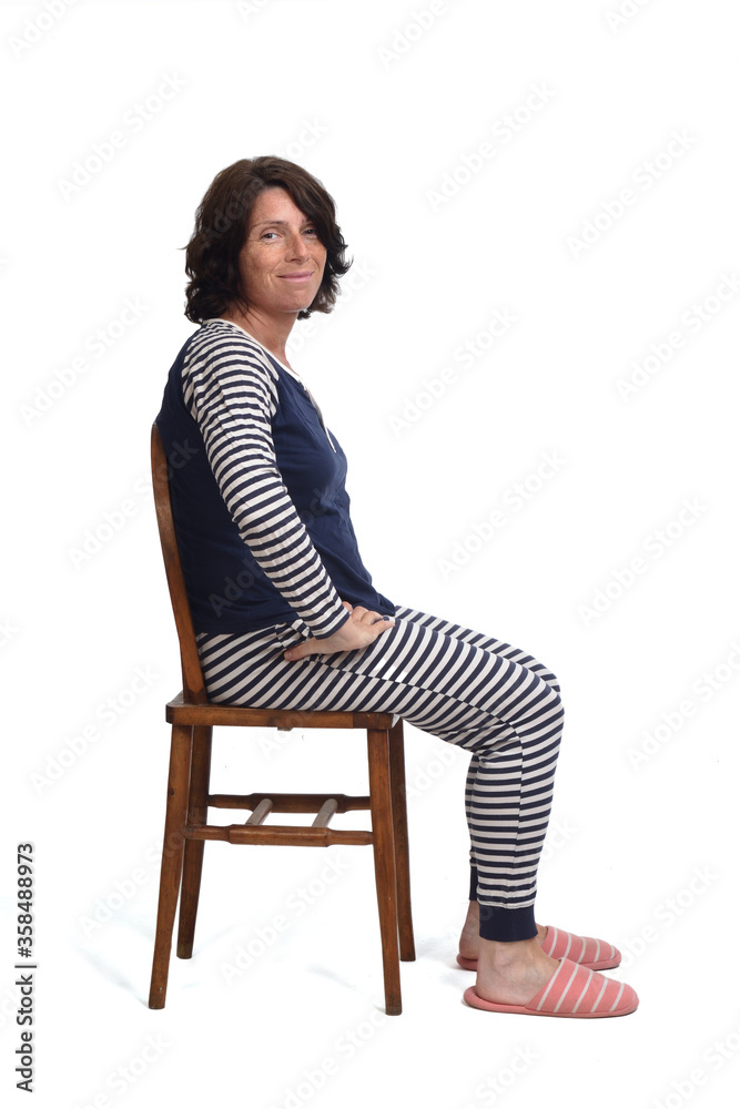 side view of a woman in pajamas sitting o a chair on white backgroun,looking at camera