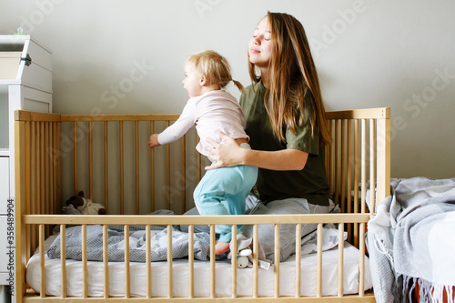 Young beautiful mother holding her toddler baby girl sitting together in a cot