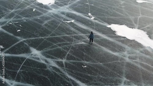 Aerial top view of a man ice skating outdoors on frozen water reservoir. Clip. Male tourist ice skating on frozen lake with thick ice with deeep cracks below his legs. photo